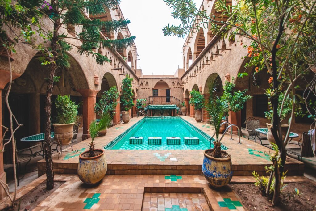 Charming pool courtyard of a traditional riad in Ouarzazate, Morocco, with lush plants and intricate architecture.